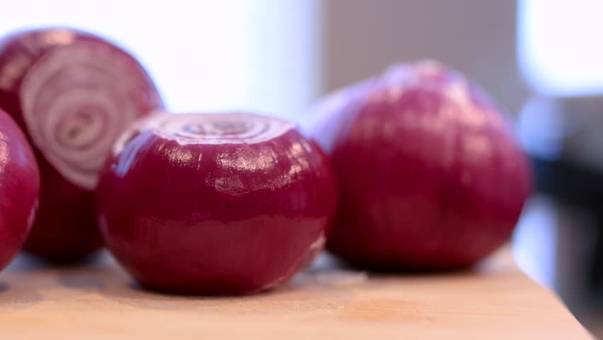 Group of whole, peeled red onions resting on a wooden board, ready for cooking preparation.