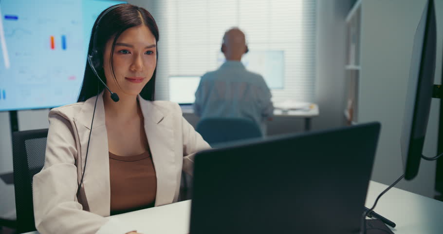Young Asian female agent talking on phone headset consulting client online in call center office. Corporate customer service, technical support, remote tech operator, business team help desk concept.