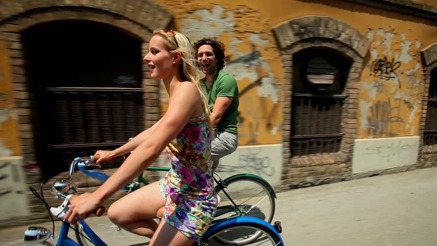 Couple cycling in town on sidewalk lane past old abandoned building  | Shutterstock HD Video #4153933