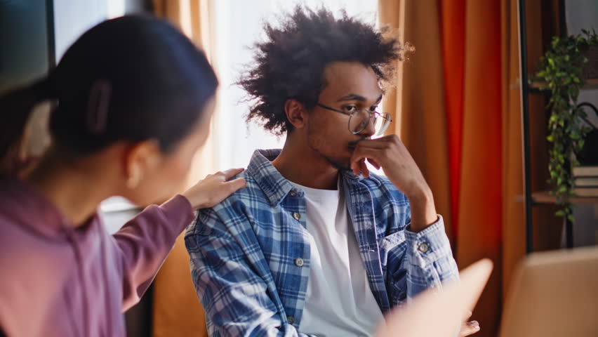Mixed race couple facing financial problems at kitchen table, asian girlfriend comforts frustrated african american boyfriend holding head in hands, diverse pair stressed over debt. Family crisis