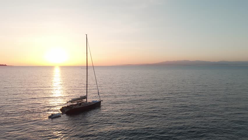 Aerial view of a sailboat anchored on calm sea at sunrise near Sardinia coastline