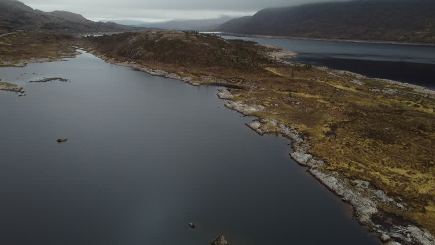 Dramatic aerial view flying along the rugged and desolate shoreline of Loch Cluanie, a reservoir in the Scottish Highlands
