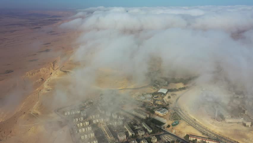 Aerial view of Mitzpe Ramon crater partially covered by low clouds over the desert town in Mitzpe Ramon, South District, Israel.