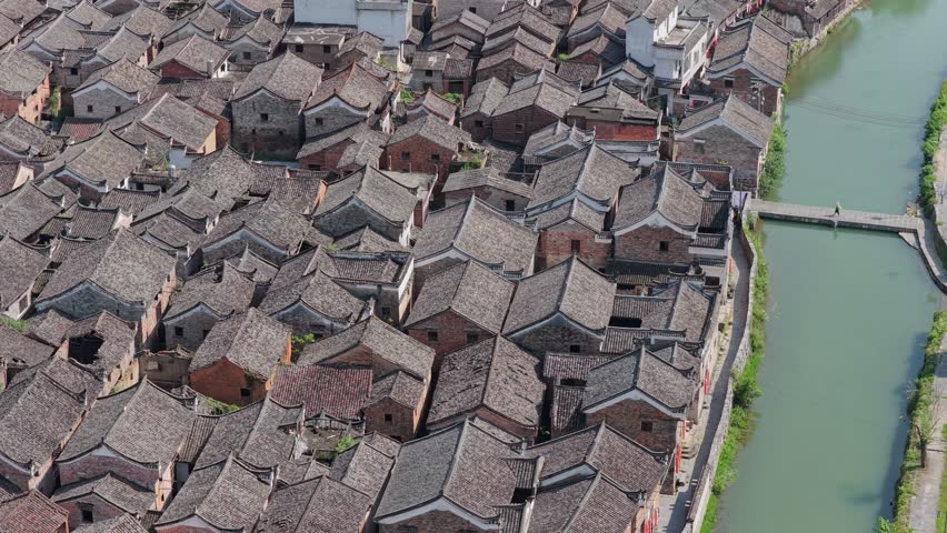 Aerial view of the historic Shanggantang ancient village with traditional grey-tiled roofs, a winding river, and a stone bridge in Yongzhou, Hunan, China.