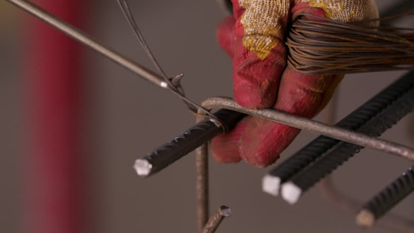 Worker tying steel reinforcement bars with binding wire close up