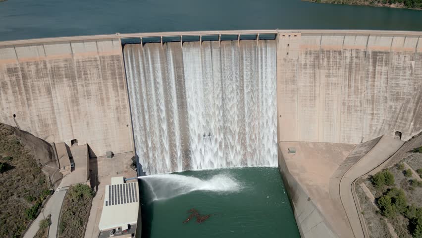 Reservoir at full capacity releasing water into the river. Aerial view. Water management at a gravity dam. Rules Dam. Spain.