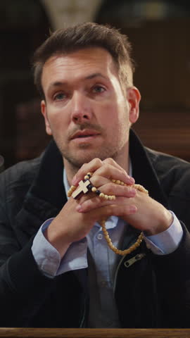 Private moment of prayer, a man sitting on a wooden pew in a peaceful, empty Christian church, praying with rosary beads.