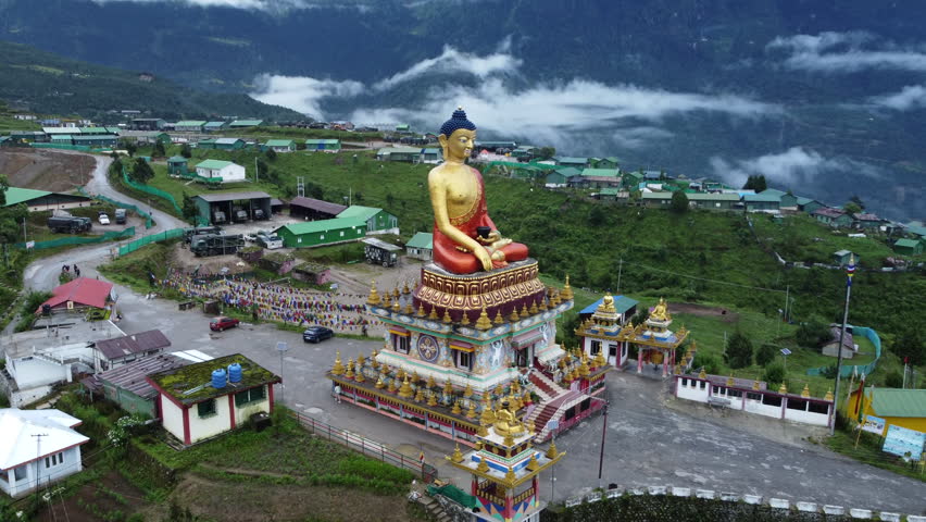 Aerial drone view of a Buddhist statue and colorful mountain settlement surrounded by mist-covered Himalayan mountains in Arunachal Pradesh, Northeast India.