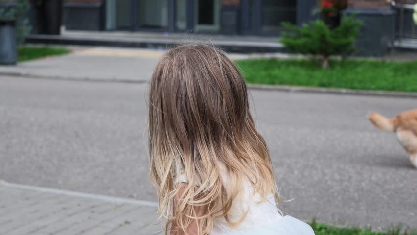 Young Girl with Blonde Hair Wearing White Lace Dress Turning to Look at Camera Outside in Urban Park Setting