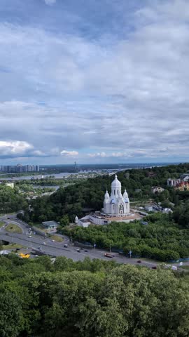 Scenic view of an orthodox church on green hills in Kyiv overlooking a highway and the Dnieper river under a cloudy sky in vertical video format