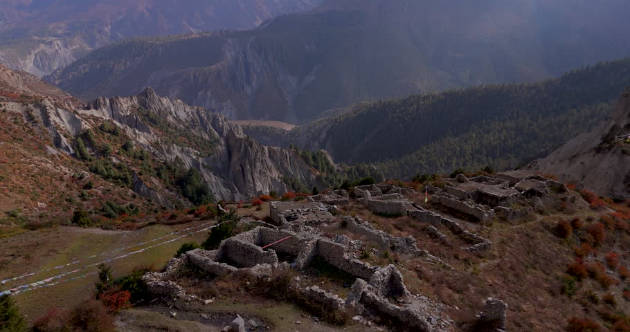 Yak Kharka, Annapurna Circuit, Manang, Nepal, gliding drone shot revealing stone house ruins on a high mountain ridge overlooking a deep Himalayan valley