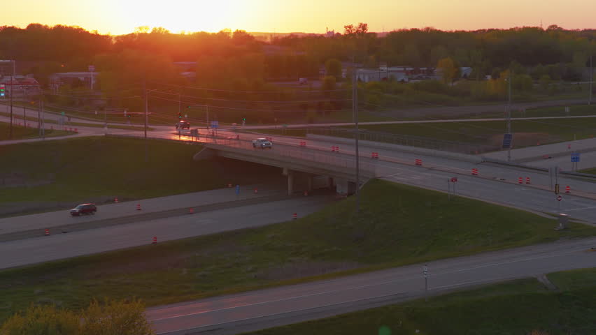 Golden hour aerial of a long-haul red semi truck crossing under a highway overpass near DeForest, Wisconsin, evoking the trucking workforce and driver shortage on the freight corridor.