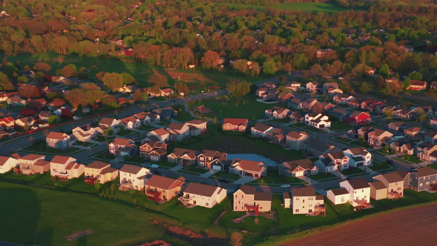 Golden hour drone view of a residential subdivision in DeForest, Wisconsin, with curving streets and homes around a small pond framed by trees and open farmland.