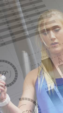 Close up of a Caucasian woman doing leg lifts in the gym. Digital animation of graphs and statistics are seen running in the foreground