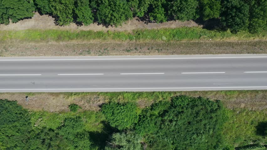 Direct overhead shot of two automobiles moving on rural road through dense green trees. Concept of road trip, transportation infrastructure, travel freedom, and scenic country driving.4K aerial shot.