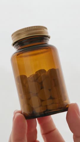 Hand holding amber glass bottle pills vitamins medicine supplements healthcare pharmacy closeup vertical video