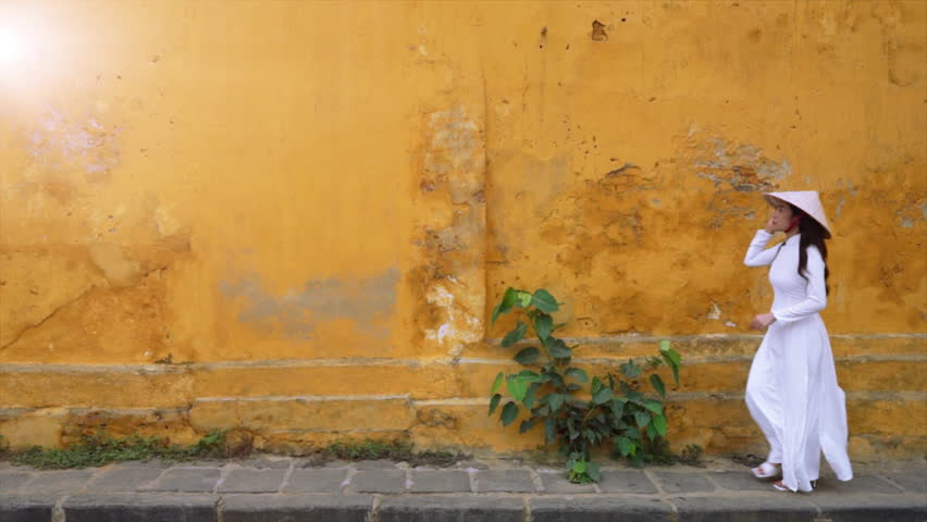Asian woman wearing traditional Vietnamese culture walks beside an old wall in Hoi An, Vietnam.