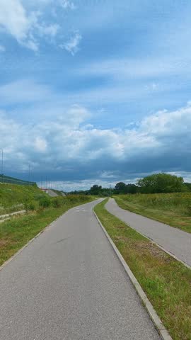 Paved bike path leading through green countryside under cloudy sky. Bicycle POV.