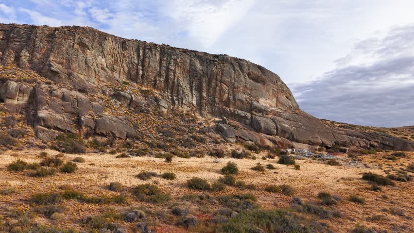 Rugged rock formation and steep cliff face under a blue sky in a dry wilderness landscape