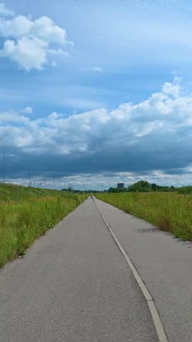 Paved bike path extending through grassy field under cloudy sky. Bicycle POV.