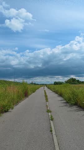 Paved path extending through overgrown grassy field under cloudy sky. Bicycle POV.