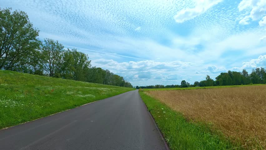 Country road stretching through green countryside under cloudy sky. Bicycle POV.