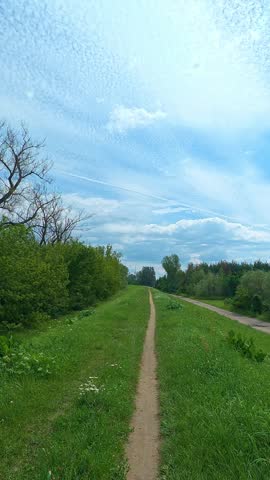 Narrow dirt path leading through grassy park embankment under cloudy sky. Bicycle POV.