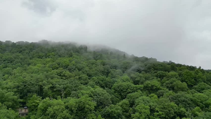 Aerial view flying over lush green mountains and low drifting clouds near Cherokee, North Carolina, with dense forest and atmospheric mist.
