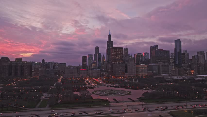 Chicago skyline at dusk with dramatic pink and purple clouds over downtown, Willis Tower and Grant Park illuminated by city lights.
