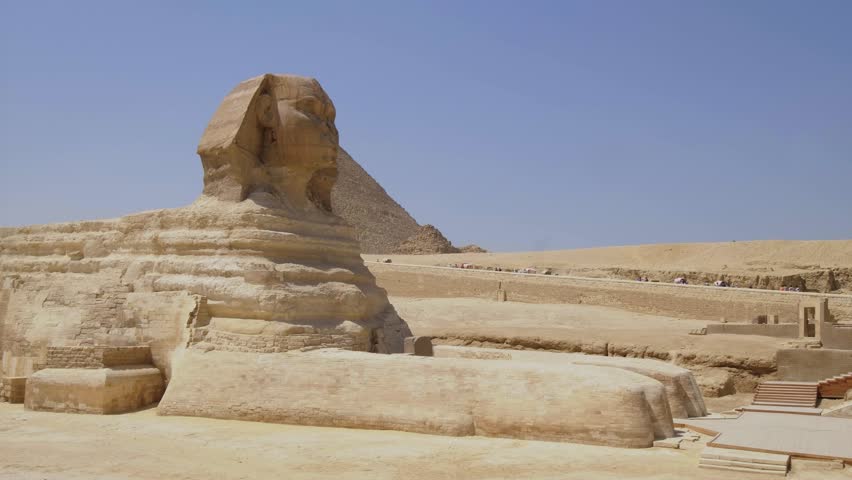 Great Sphinx of Giza with an ancient pyramid in the background under a clear blue sky in Egypt.
