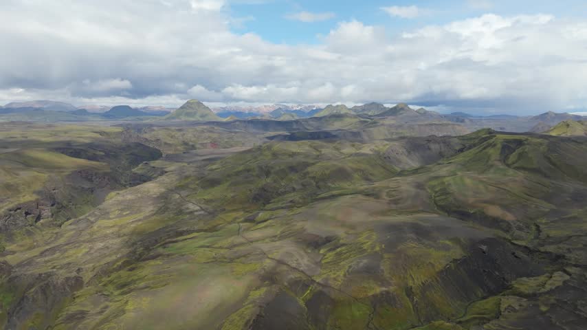 Aerial push in drone shot over the vast, rugged volcanic landscape of the Laugavegur hiking trail on Iceland. Serene beauty of moss-covered hills and the Hattafell mountain under a cloudy sky.