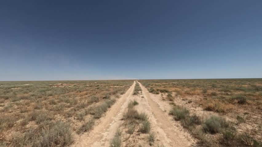 Off-road vehicle navigates a dusty trail through an expansive landscape under a clear blue sky, showcasing the rugged terrain and vegetation