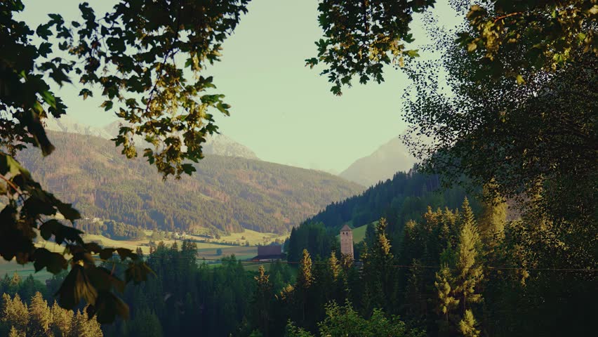 A stone tower rises from dense pine forests in mountain valley.