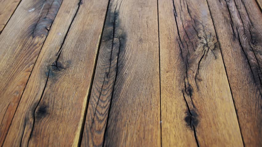 Close up camera motion over a large treated wooden board, highlighting detailed natural wood grain, cracks, and rustic timber texture.