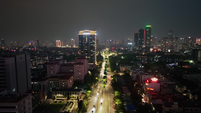 Elevated nighttime view of illuminated Hanoi traffic along Ring Road 2.7 beside Nghia Do Lake, featuring urban architecture, residential districts, and a glowing city skyline.
