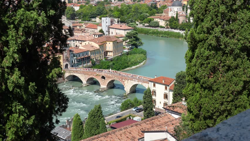 View of Ponte Pietra spanning the Adige River in Verona, Italy, framed by historic architecture and lush greenery on a sunny day