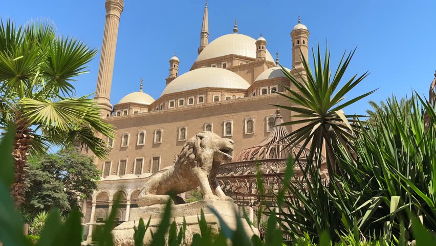 Islamic architecture of Muhammad Ali Mosque with domes, minarets and lion statue in the green bushes of Citadel courtyard