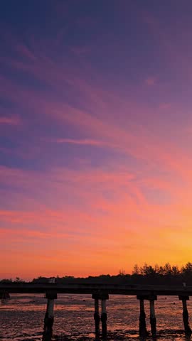 Silhouetted pier against a vibrant sunset sky over calm waters.
