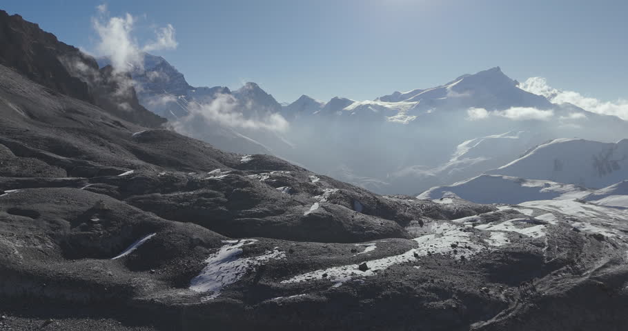 Annapurna Circuit, Manang region, Nepal, drone shot of rocky mountain ridges and snow-covered slopes with clouds drifting around Himalayan mountain peaks under morning sunlight