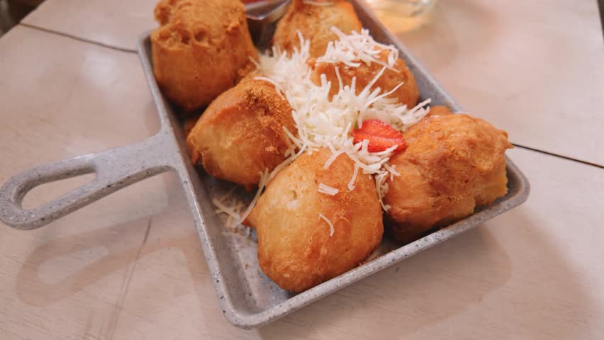 Crispy fried food balls served in a small metal dish topped with grated cheese.