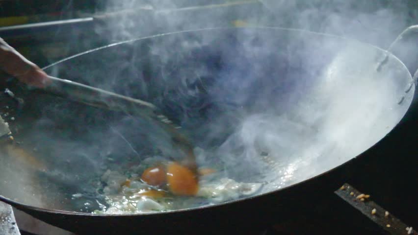 Chef cooking egg for delicious street food in a large wok with steam rising.