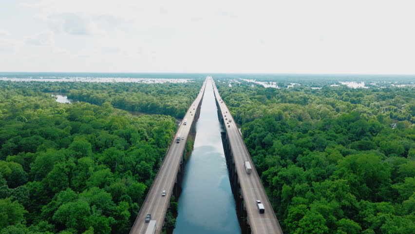 Symmetrical aerial down the twin spans of the Atchafalaya Basin Bridge, I-10 traffic vanishing to the horizon above the Louisiana swamp and river channel.