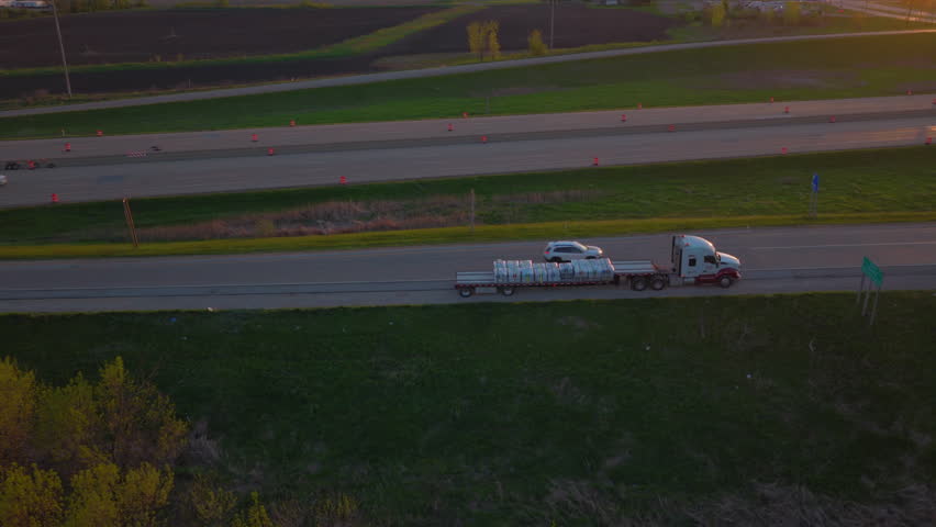 Elevated aerial clip showing a stalled flatbed truck carrying wrapped cargo parked on the shoulder ramp of the highway during sunset in Wisconsin.