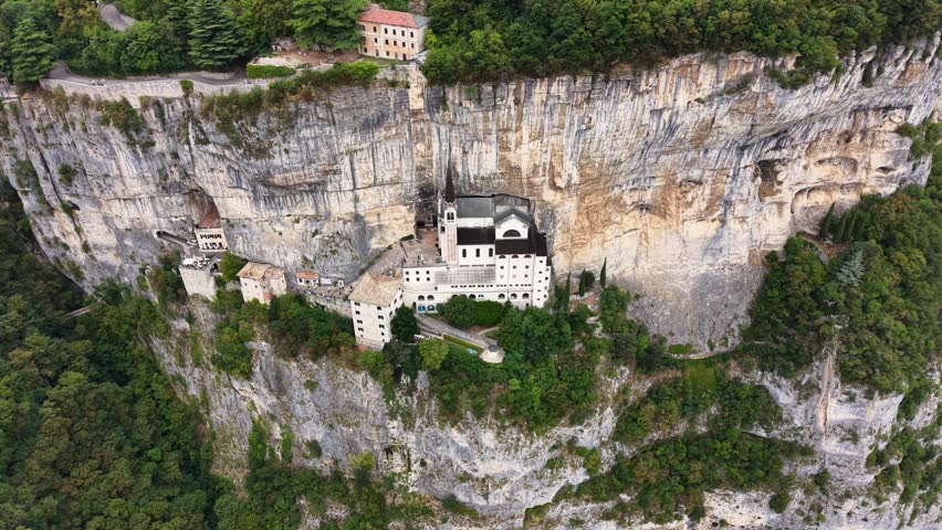 Drone view of Santuario Madonna della Corona nestled beneath towering limestone cliffs in northern Italy