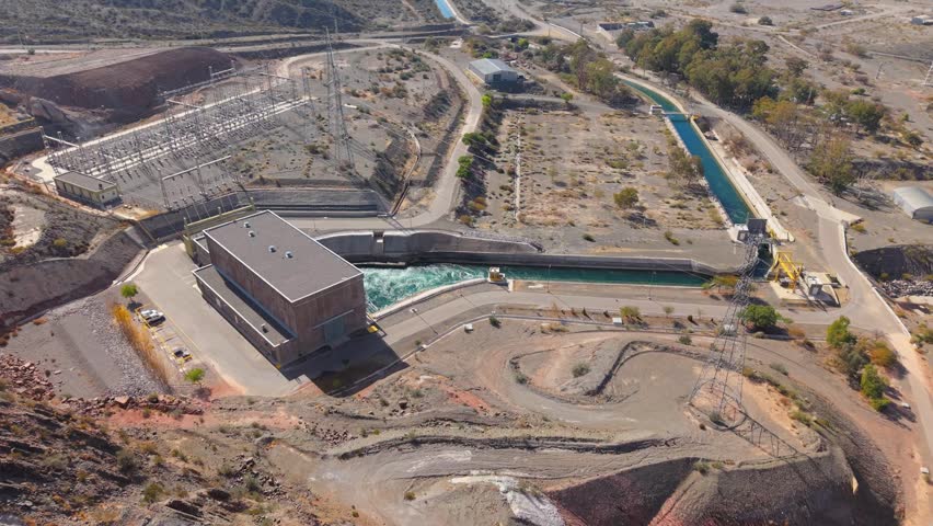 Punta Negra Hydroelectric Power Station on the Zonda River, Ullum, San Juan, Argentina, showing the powerhouse, switchyard, tailrace channel and transmission facilities, drone establishing shot.