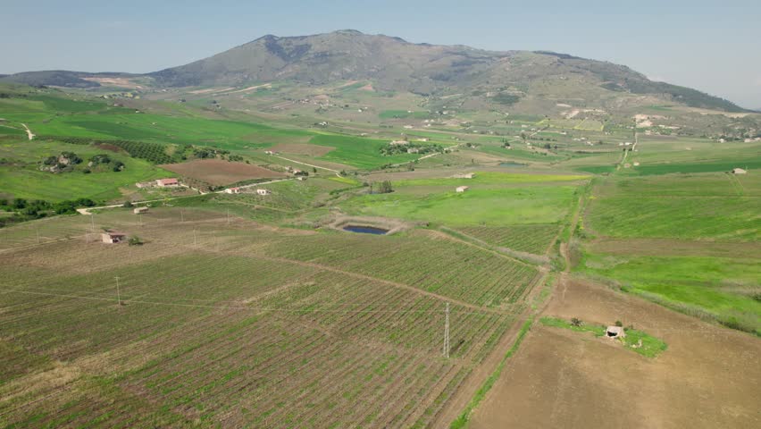 Aerial footage shows a lone farmhouse and small pond surrounded by green fields below Sicilian hills.