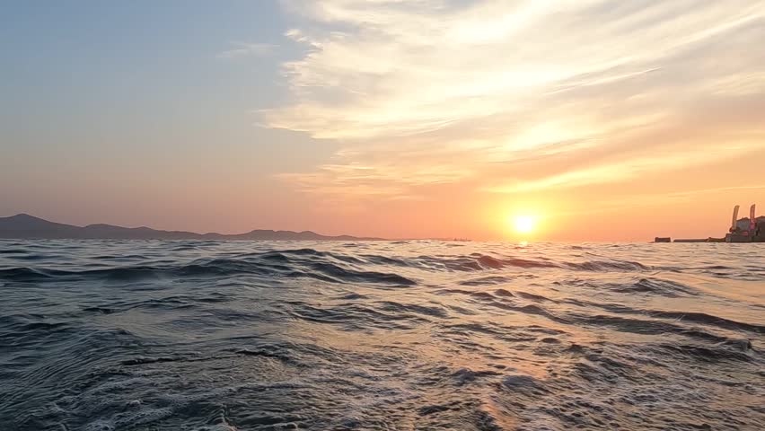 Scenic sunset over Adriatic sea with warm orange sky, rippling water, and coastal shoreline. Peaceful Croatian seaside scene, tourism, and Mediterranean lifestyle.