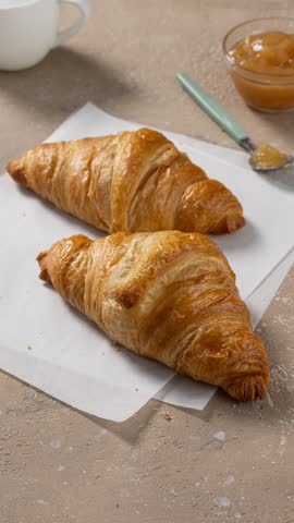 Stop motion video of two freshly baked croissants and a small bowl of jam arranged on a cozy kitchen breakfast table. The croissants move playfully across the table, creating a warm and appetizing breakfast scene