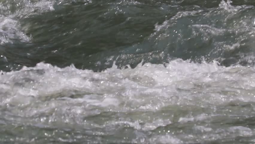 Close aerial view of fast river rapids churning dark water and white foam swirling over rocks and currents