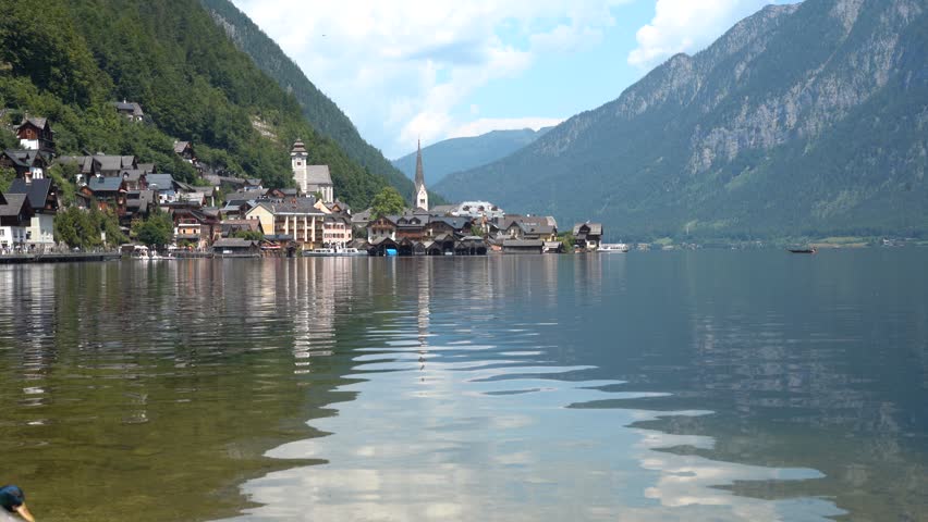 Calm in Hallstatt Village on Lake Alpine Mountains and water waves in Austria. Old houses. Green hill background.